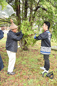 写真1：現地で針葉樹の枝を採取する、エド・キャリア氏（左）。<br>Photo1 : Mr. Ed Carriere (left） cutting the softwood branch.